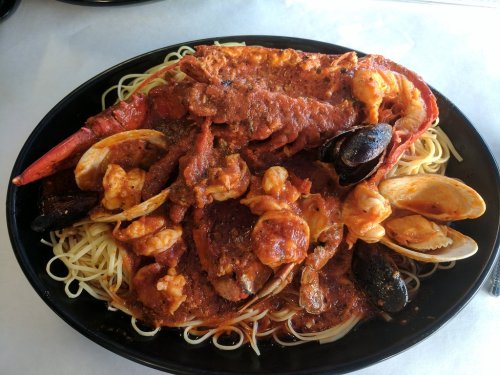 A large platter of seafood pasta featuring lobster, shrimp, clams, and mussels in a rich tomato sauce.