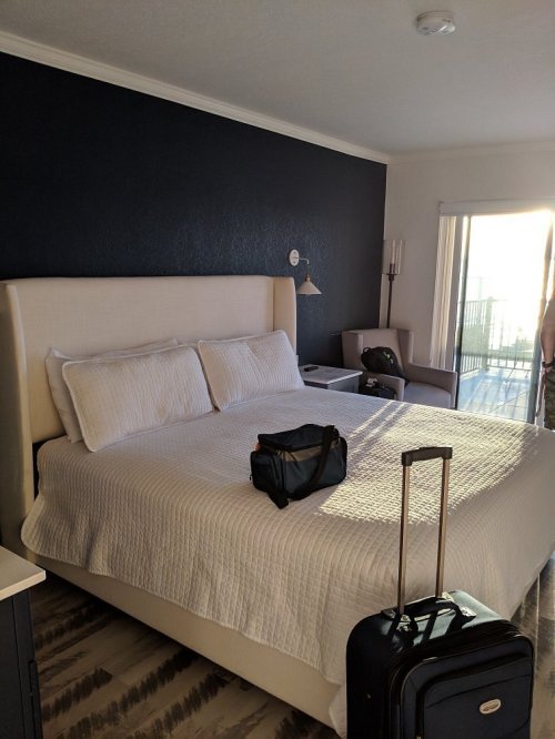A cozy hotel room with a large bed, a suitcase, and a view of a balcony through glass doors.