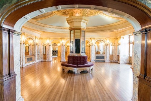 Elegant interior of a grand room featuring ornate architecture, marble details, and a central seating area.