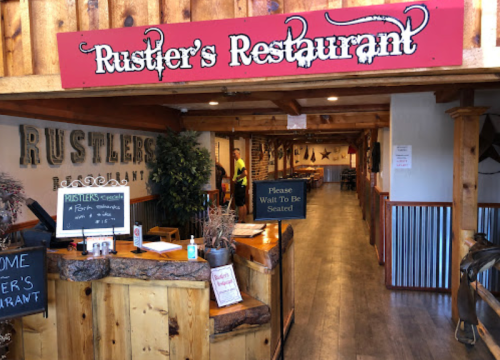 Entrance of Rustler's Restaurant featuring a wooden decor, a sign to wait to be seated, and a welcoming atmosphere.