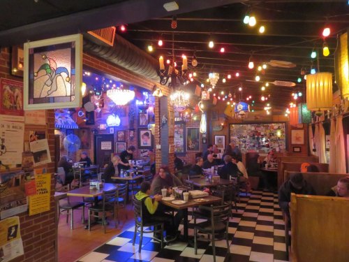 A cozy restaurant interior with colorful lights, checkered floors, and patrons enjoying meals at various tables.