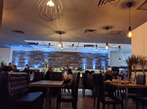 A cozy restaurant interior with dim lighting, wooden tables, and plants, featuring a modern design and a relaxed atmosphere.