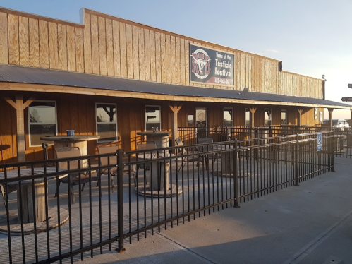 Exterior of a wooden building with a sign for the Testicle Festival, featuring outdoor seating and a fenced area.