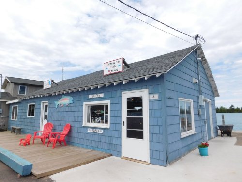 A blue wooden building with a sign reading "Jamman's Fish Market," featuring red chairs on a deck by the water.