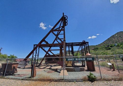 A rusted mining headframe structure at Audrey Headframe Park, surrounded by a fence and desert landscape.