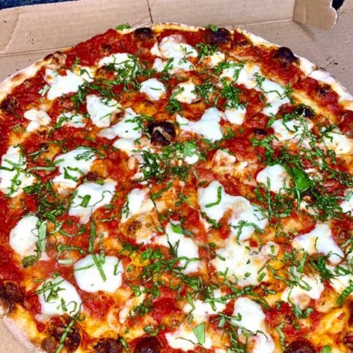 A freshly baked pizza topped with tomato sauce, mozzarella cheese, and fresh basil, in a pizza box.