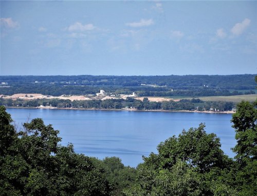 A serene lake view with lush greenery in the foreground and distant hills under a clear blue sky.