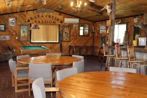 Interior of a rustic saloon with wooden tables, a pool table, and decor featuring mounted animal heads.