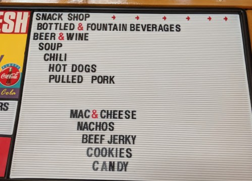 Menu board listing snacks and beverages: beer, wine, soup, chili, hot dogs, pulled pork, mac & cheese, nachos, and candy.