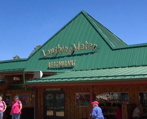 Sign for Laughing Water Restaurant with a green roof and clear blue sky in the background. People are outside.