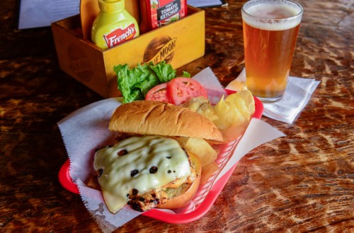 A sandwich with melted cheese, lettuce, and tomato, served with chips and a glass of beer on a wooden table.