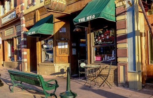 Exterior of a restaurant called "The Keg," featuring green awnings, a bench, and a small outdoor seating area.