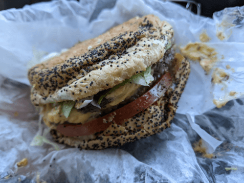 A poppy seed bun sandwich with a beef patty, cheese, lettuce, and tomato, resting on crumpled paper.
