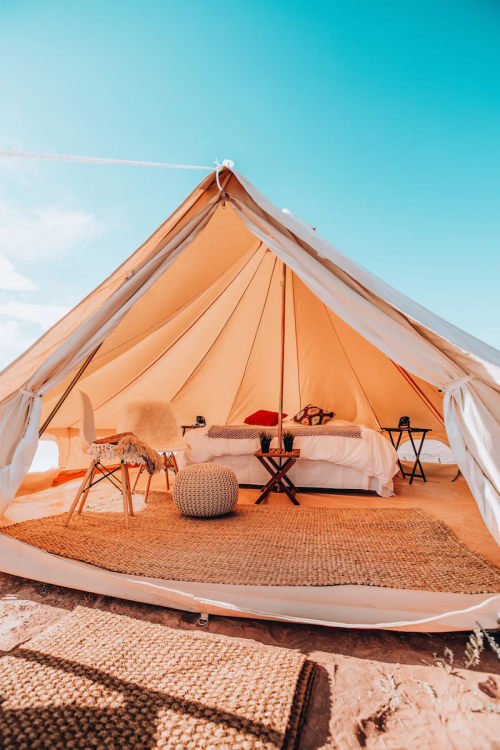 A cozy glamping tent with a bed, chairs, and decor, set against a bright blue sky.