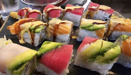 A colorful assortment of sushi rolls, featuring various toppings and fillings, arranged on a black plate.