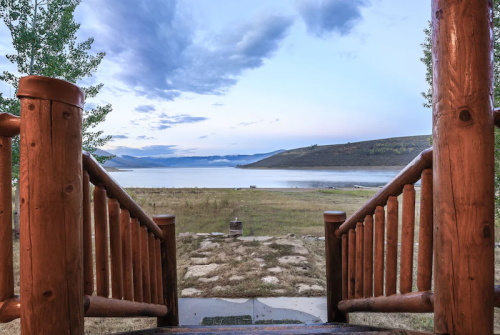 View from wooden steps leading down to a serene lake surrounded by hills under a cloudy sky.