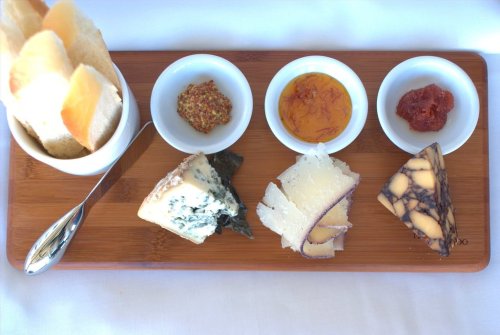A wooden platter with various cheeses, dips, and crackers arranged neatly.