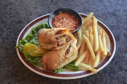 A plate with two rolled sandwiches, fries, a small bowl of marinara sauce, and a pepper on a bed of lettuce.