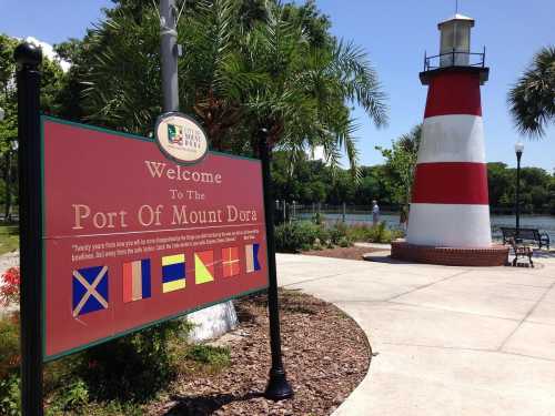 Sign welcoming visitors to the Port of Mount Dora, featuring a red and white lighthouse and palm trees in the background.