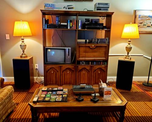 A vintage entertainment center with a TV, game console, and shelves of games, flanked by lamps and speakers.