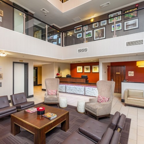 Modern lobby area with seating, a coffee table, and a reception desk, featuring artwork on the walls and natural light.