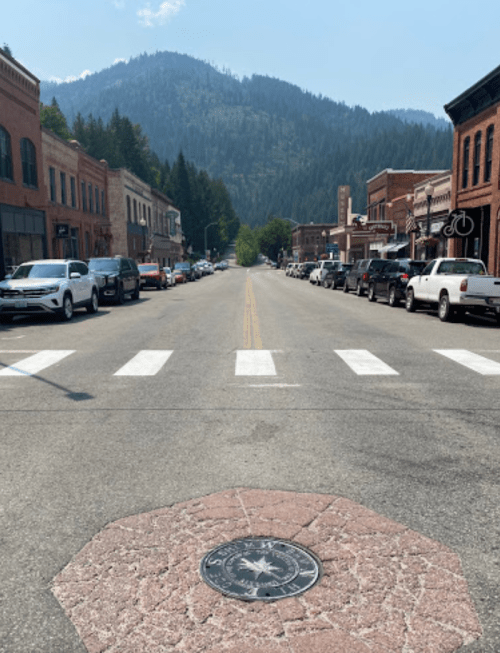 A quiet street lined with parked cars, leading to a mountain backdrop under a clear blue sky.