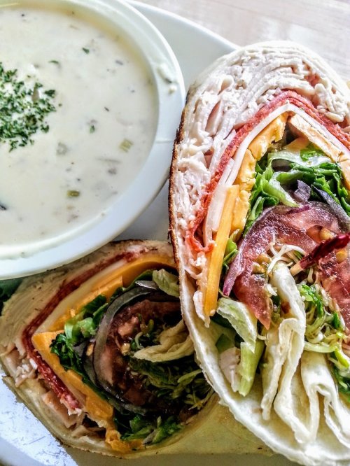 A close-up of a sandwich filled with meats and vegetables, alongside a bowl of creamy soup.