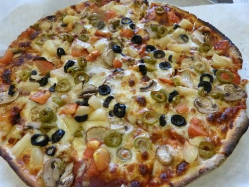 A freshly baked pizza topped with cheese, mushrooms, tomatoes, olives, green peppers, and pineapple.