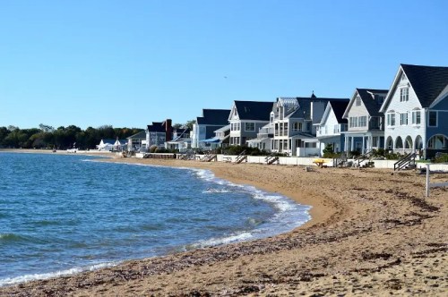 A sandy beach lined with charming houses under a clear blue sky and calm water.