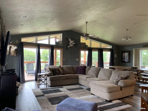 Spacious living room with a large sectional sofa, windows, and a view of a deck surrounded by greenery.