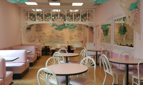 A pastel-colored café interior with pink booths, round tables, and whimsical wall murals of trees and landscapes.