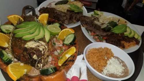 A vibrant platter of grilled fish garnished with avocado, lime, and oranges, accompanied by rice and beans.