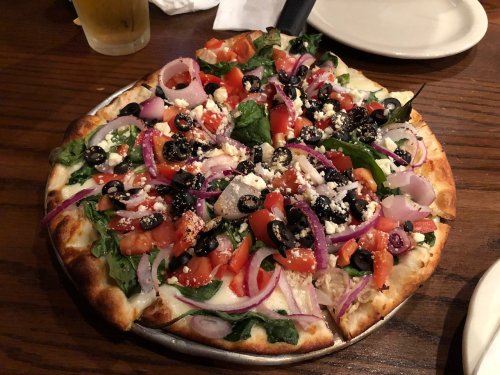 A fresh vegetable pizza topped with spinach, tomatoes, olives, red onions, and feta cheese on a crispy crust.