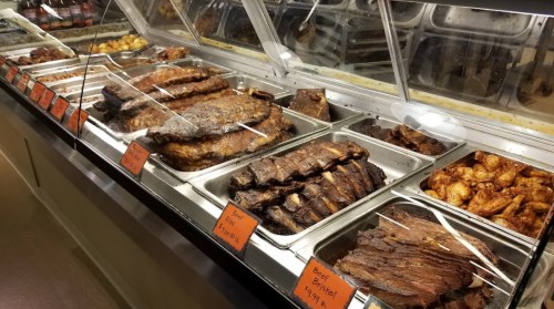 A display of various meats, including ribs, brisket, and chicken wings, in a buffet setting with price tags.
