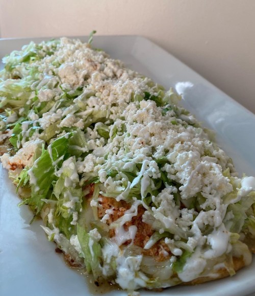 A plate of enchiladas topped with shredded lettuce and crumbled cheese, drizzled with creamy sauce.