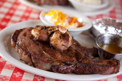 A plate featuring a grilled steak topped with shrimp, served with a side of baked potato and cheese.