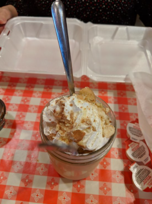A glass jar filled with whipped cream and crumbled cookies, sitting on a red checkered tablecloth.