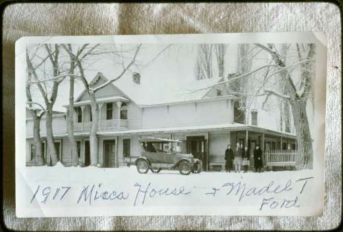 Black and white photo of a house from 1917 with a vintage Ford car and four people standing in front.