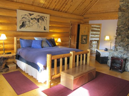 Cozy log cabin bedroom with a wooden bed, stone fireplace, and warm lighting, featuring rustic decor and a welcoming atmosphere.