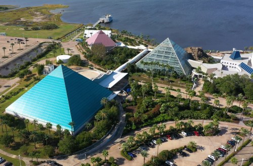 Aerial view of colorful pyramids surrounded by greenery and a parking lot near a body of water.