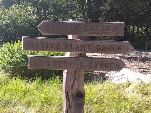 Wooden signpost with three arrows pointing to "Visitor Center," "Native Plant Garden," and "Butterfly Garden."