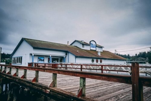 A blue and white building with a sign reading "Moe's," situated on a wooden pier under a cloudy sky.