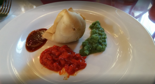 A plate with a samosa and three types of chutney: red, green, and a dark sauce.