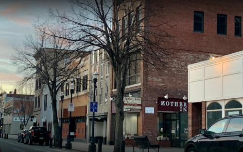A street view of buildings with trees, featuring a sign for "Mother Inn" and parked cars.