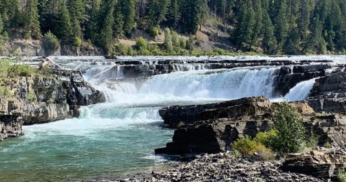 A scenic view of cascading waterfalls surrounded by lush greenery and rocky formations.