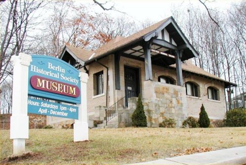 A brick building with a sloped roof, featuring a sign for the Berlin Historical Society Museum and landscaped grass.