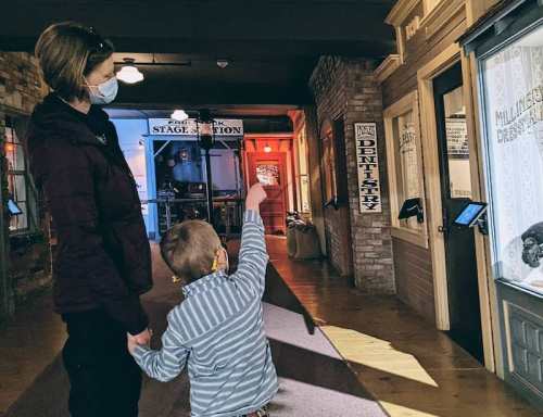 A woman and a child wearing masks explore a museum, with the child pointing at an exhibit.