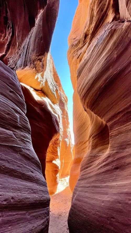 A narrow canyon with smooth, colorful rock walls and a bright blue sky visible at the top.