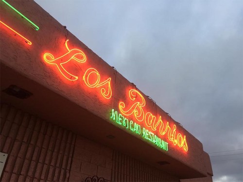 Neon sign for "Los Barrios Mexican Restaurant" against a cloudy sky.