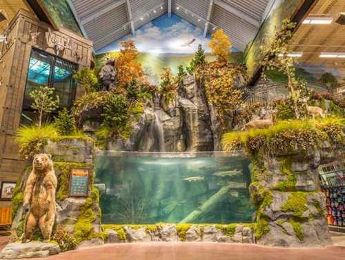 A scenic indoor display featuring a waterfall, rocks, trees, and a bear statue, creating a natural habitat atmosphere.